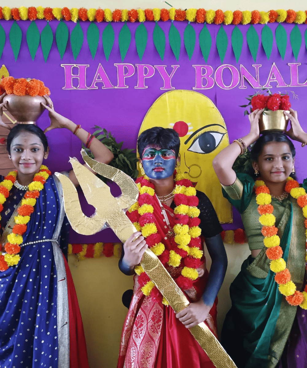 Three students dressed in vibrant traditional costumes celebrating the Bonalu festival at Guru Dronacharya Pathshala.