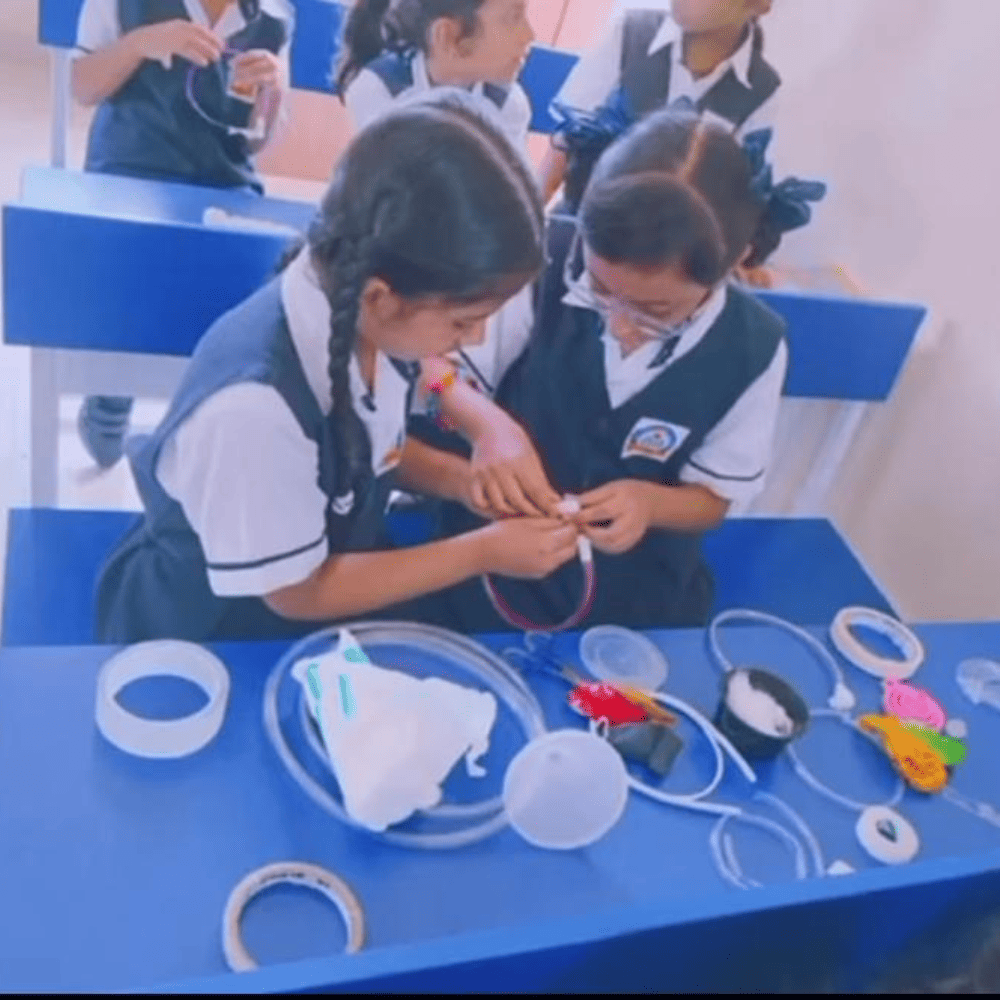 Two students collaborating on a hands-on craft or science project at their desk in the classroom.