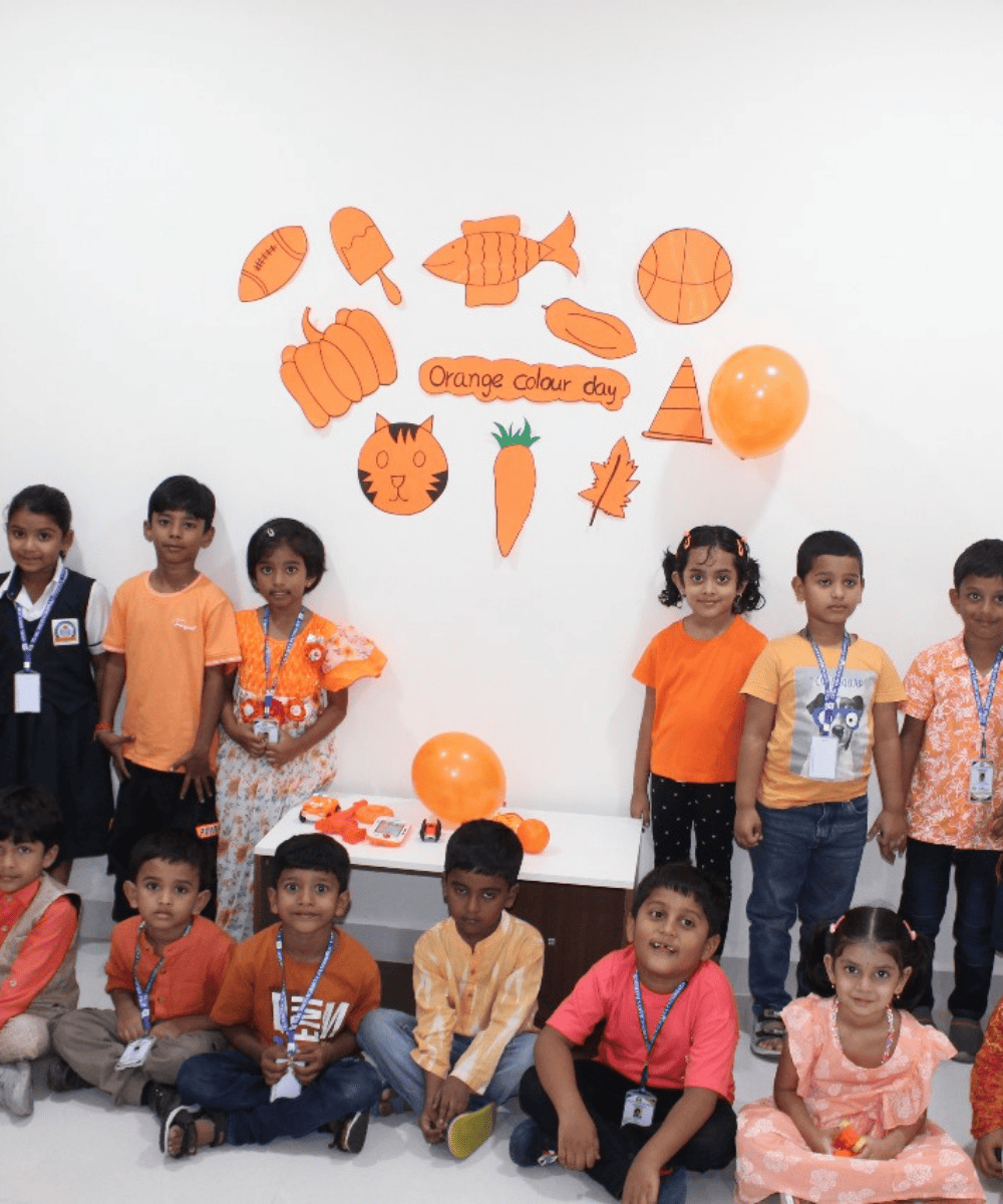 A large group of students and teachers celebrating "Orange Colour Day" with themed decorations and activities.