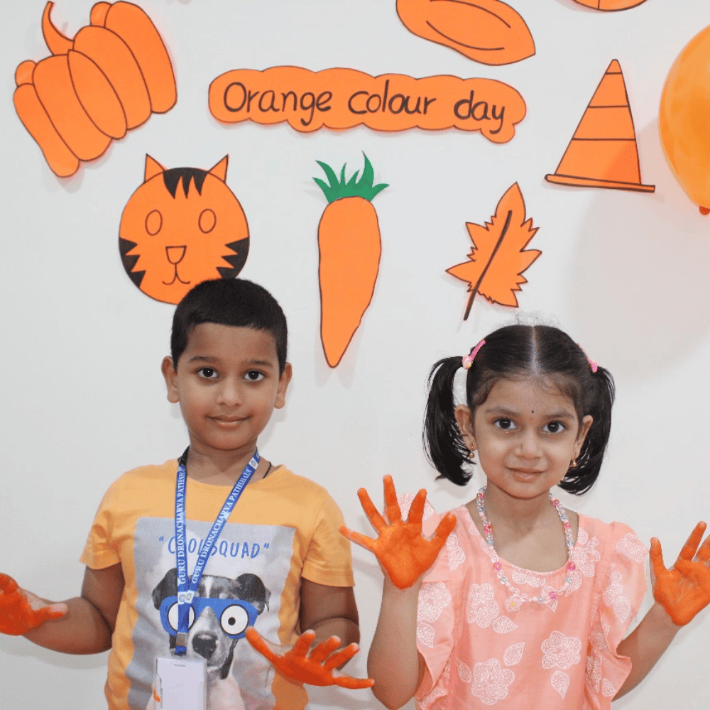 Two happy preschool students with orange painted hands celebrating "Orange Colour Day" at school.