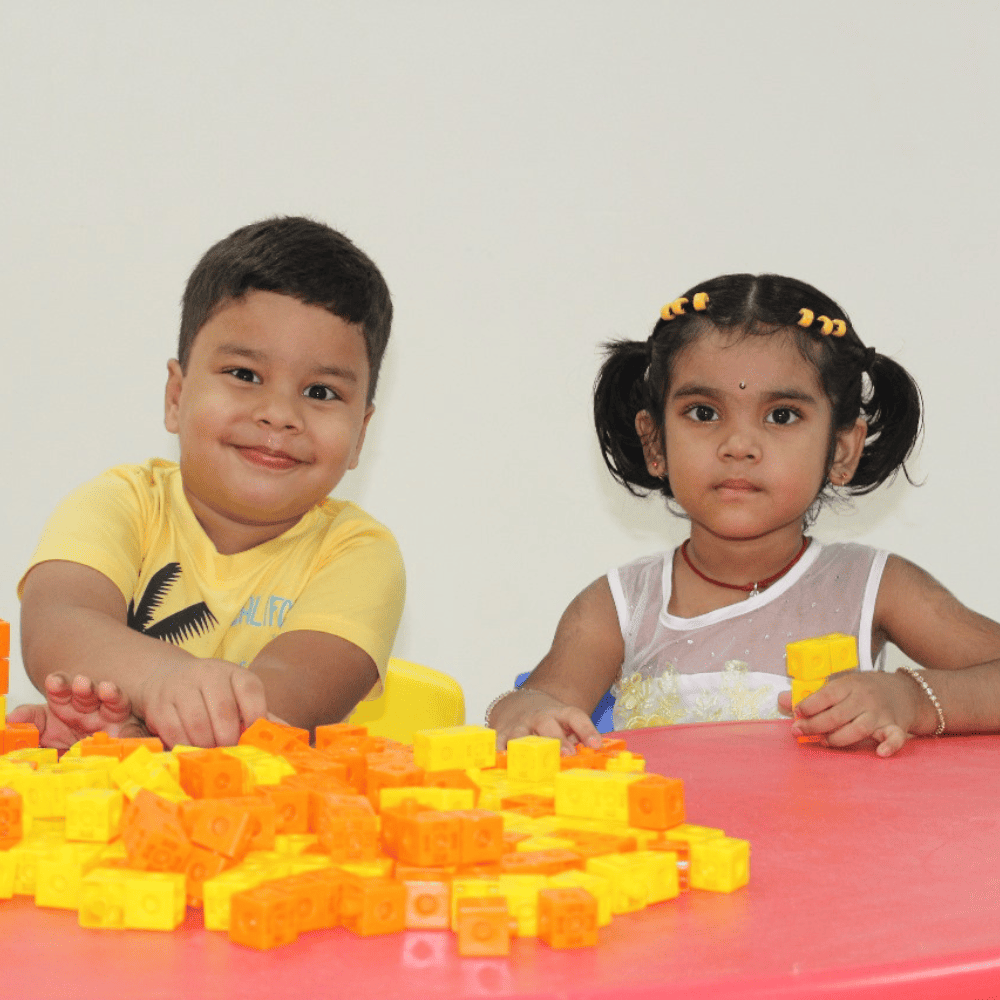 Two preschool students at Guru Dronacharya Pathshala enjoying play-based learning with colorful blocks at a table.