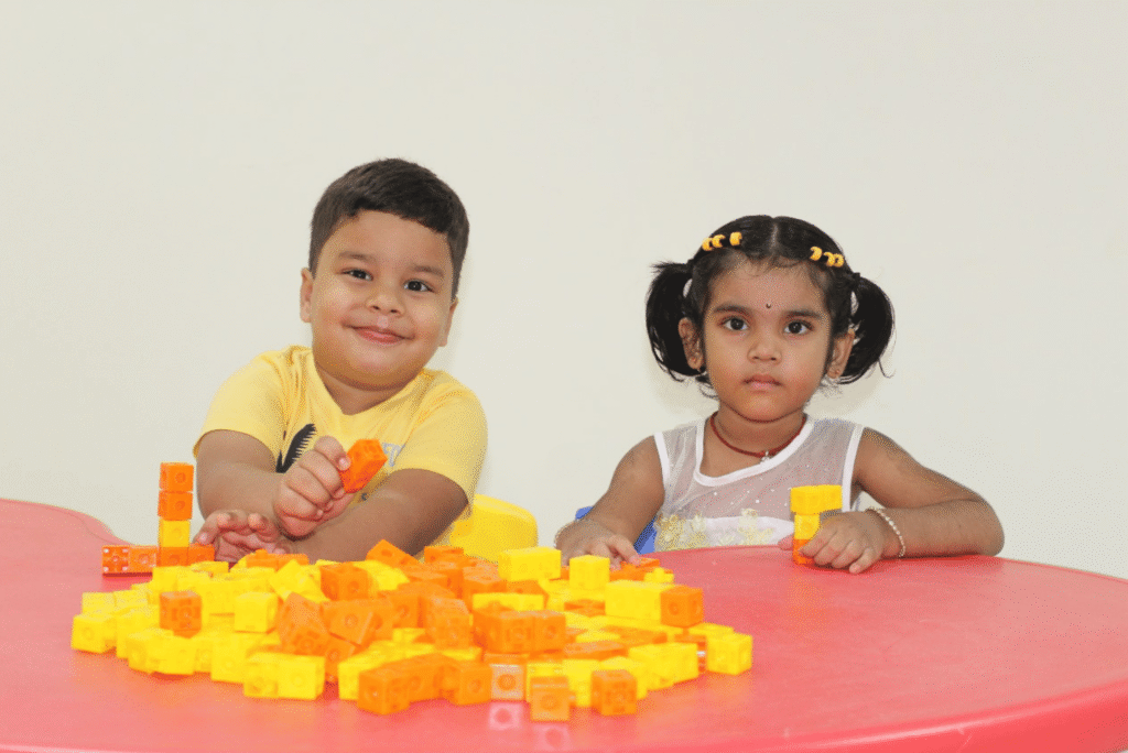 Two preschool students at Guru Dronacharya Pathshala enjoying play-based learning with colorful blocks at a table.