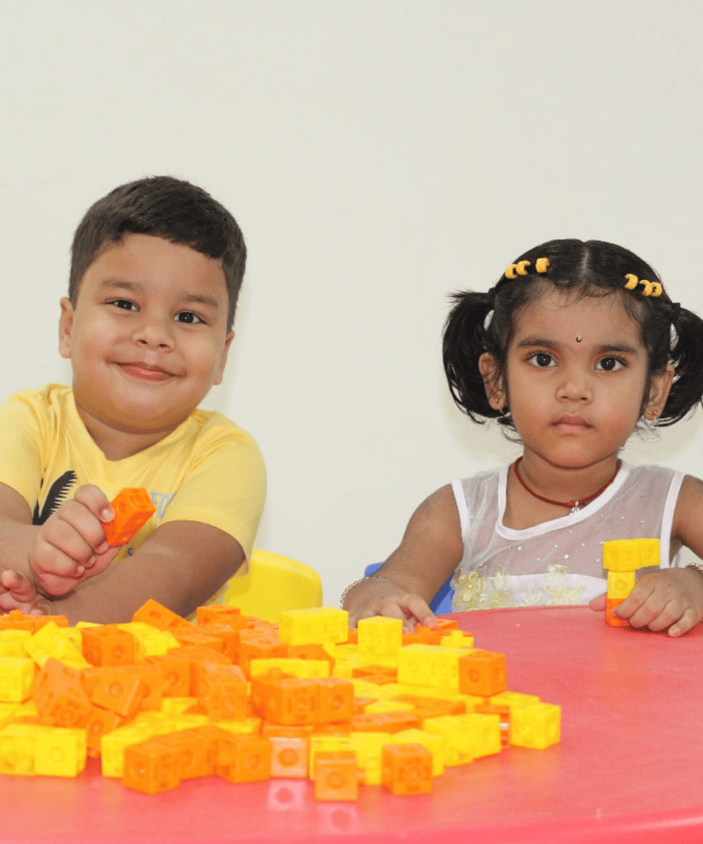 Two preschool students at Guru Dronacharya Pathshala enjoying play-based learning with colorful blocks at a table.