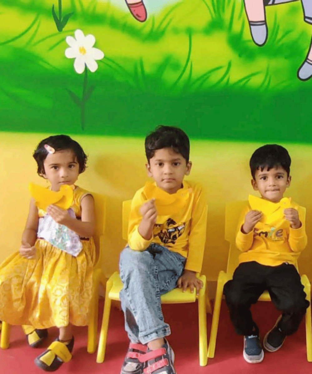 Three preschool students from Guru Dronacharya Pathshala dressed in yellow for a classroom color day activity.