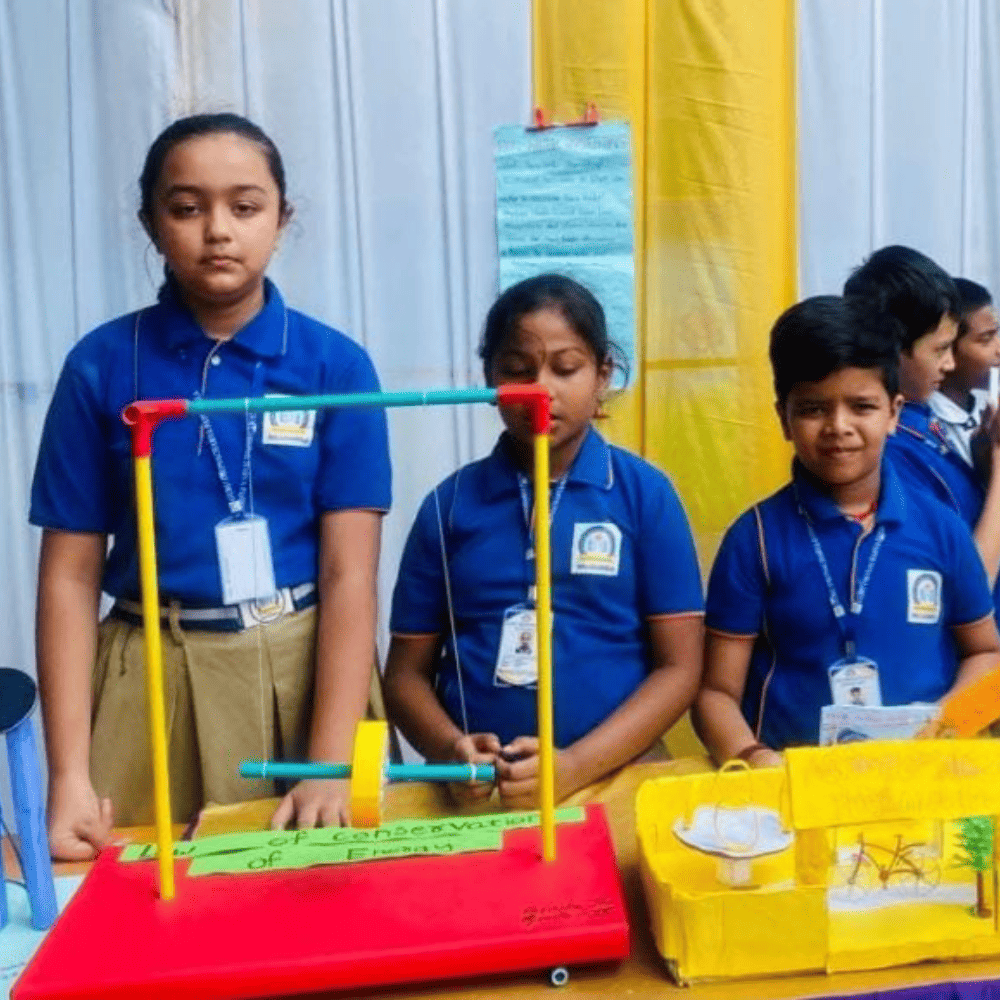 Three students proudly presenting their science fair project on the conservation of energy at Guru Dronacharya Pathshala.