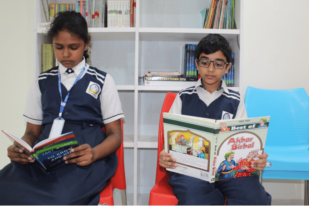 Two students in the Guru Dronacharya Pathshala library, focused on reading books to improve their knowledge and vocabulary.