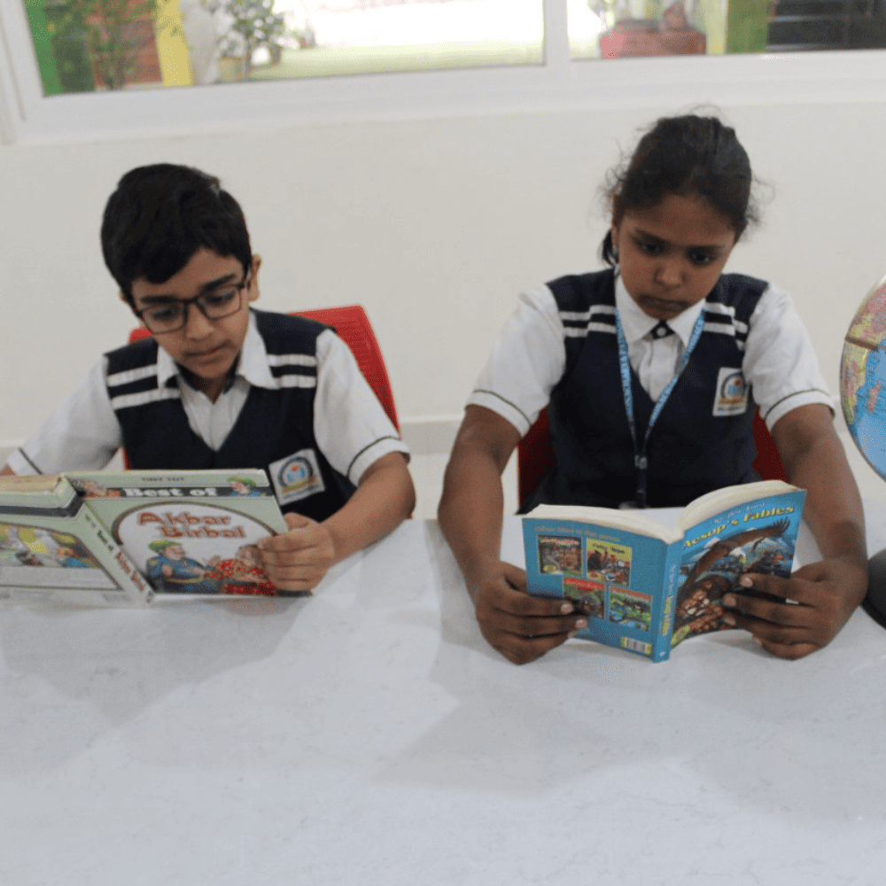 Two students in the Guru Dronacharya Pathshala library, focused on reading books to improve their knowledge and vocabulary.