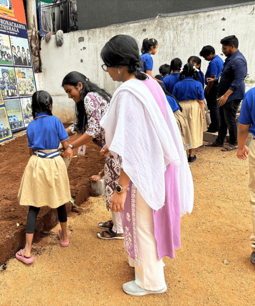 A teacher assisting a student during a hands-on outdoor gardening activity at Guru Dronacharya Pathshala.